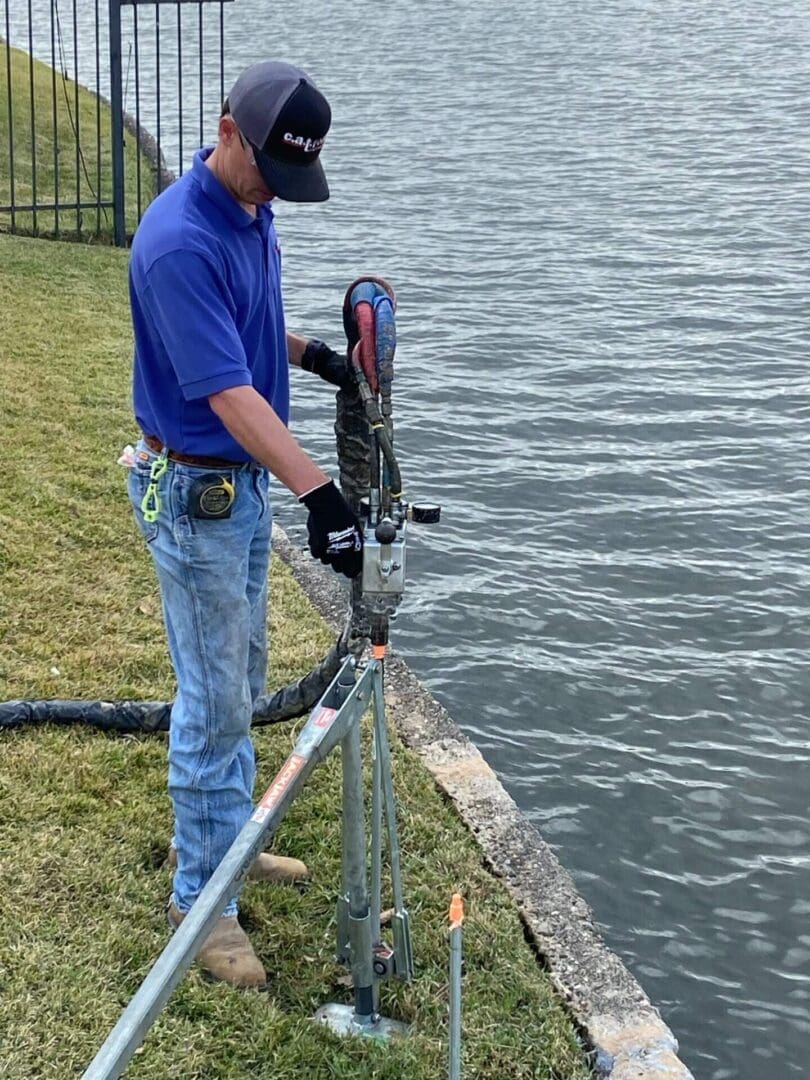 Man in blue shirt working with a tool near water.