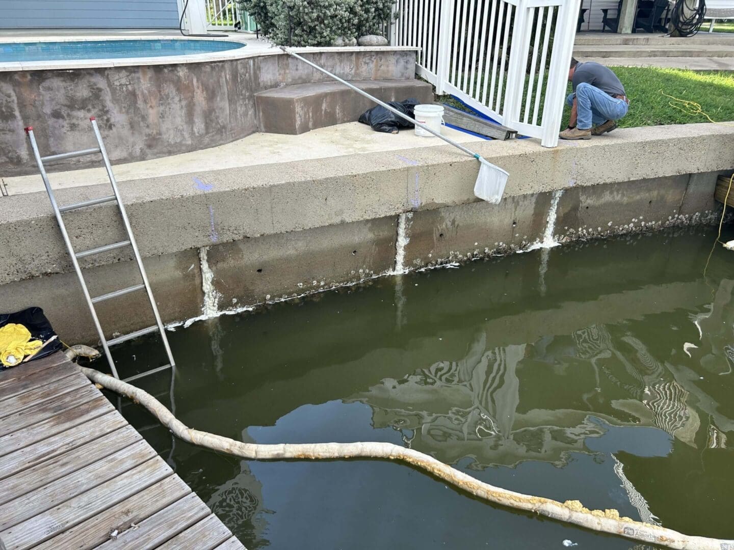 Person cleaning an empty pool with water hose and ladder visible.